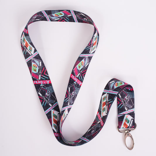 A lanyard with a colorful VHS pattern. There are three VHS tapes featured. Deep Dive, Movies with Mikey and Misc Catawampus. The Filmjoy logo is present throughout. 