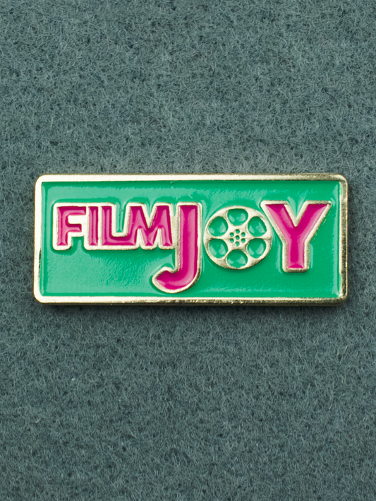 An enamel pin featuring the Filmjoy logo. Teal background with Pink text.